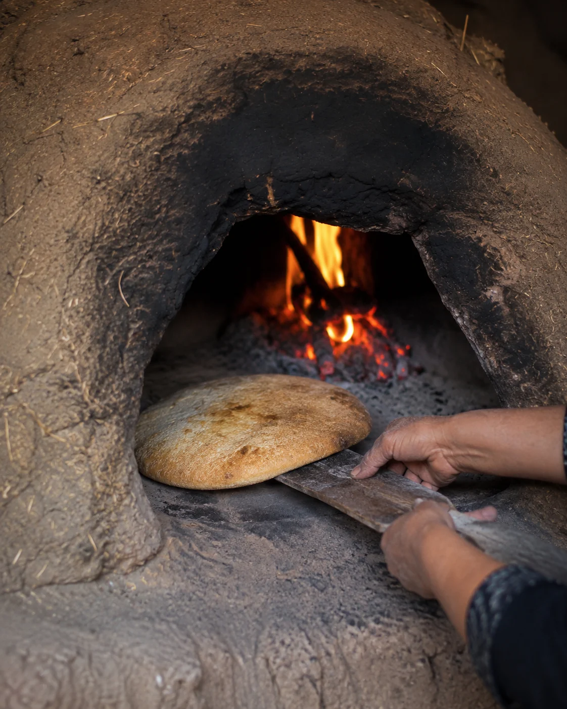 Hands turning bread carefully inside a traditional clay oven
