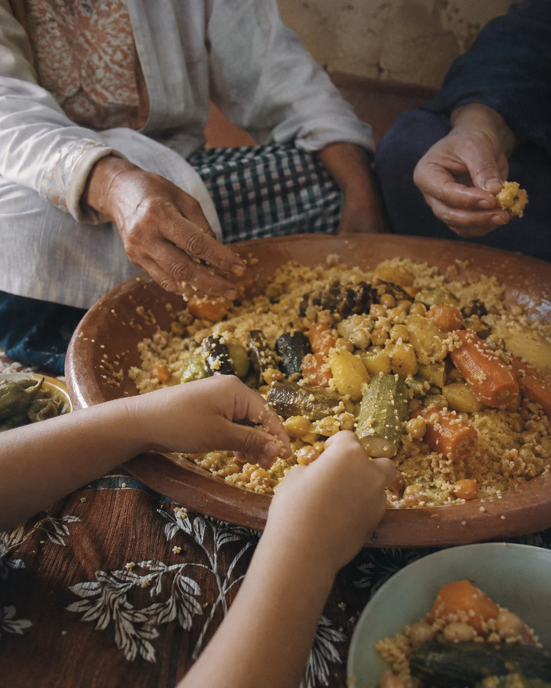 Hands trying to gather small couscous grains from a shared dish
