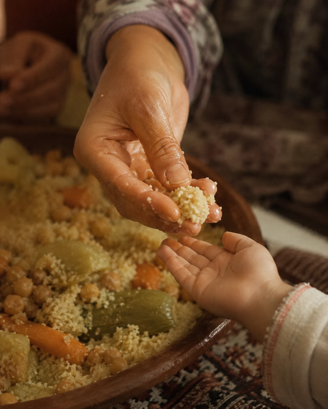 A mother's hand shaping a small couscous bite for a child