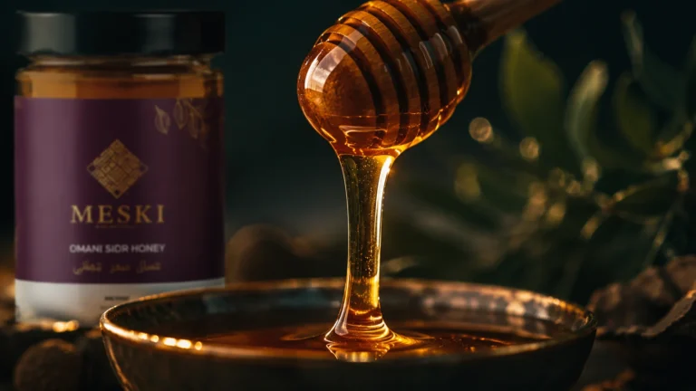 Golden Sidr honey flowing slowly from a honey dipper against a dark green background