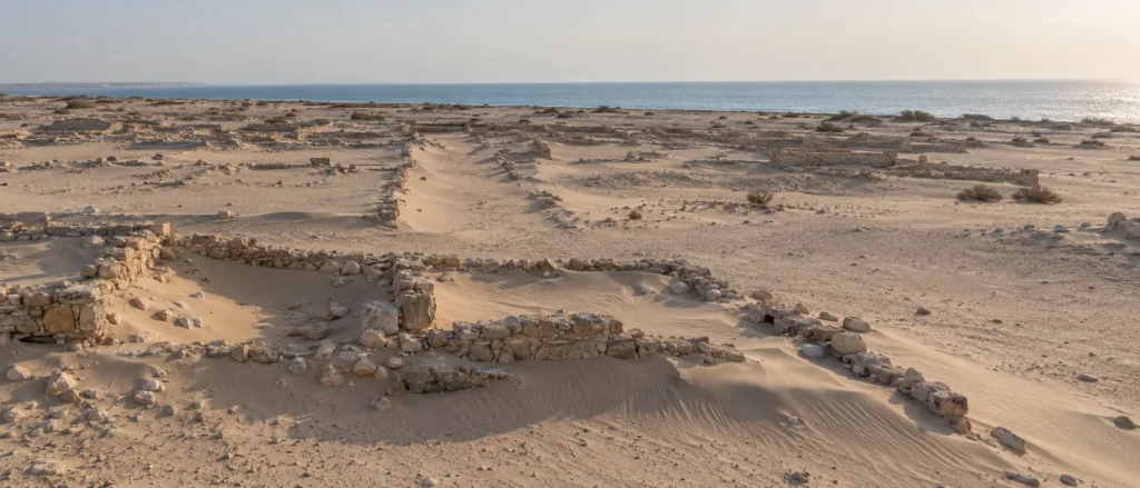 بقايا مدينة الزبارة الأثرية على ساحل قطر مع الرمال والجدران الحجرية المنخفضة الممتدة نحو البحر