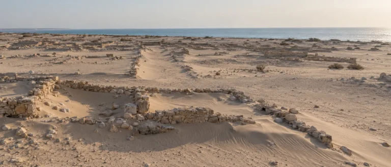 بقايا مدينة الزبارة الأثرية على ساحل قطر مع الرمال والجدران الحجرية المنخفضة الممتدة نحو البحر